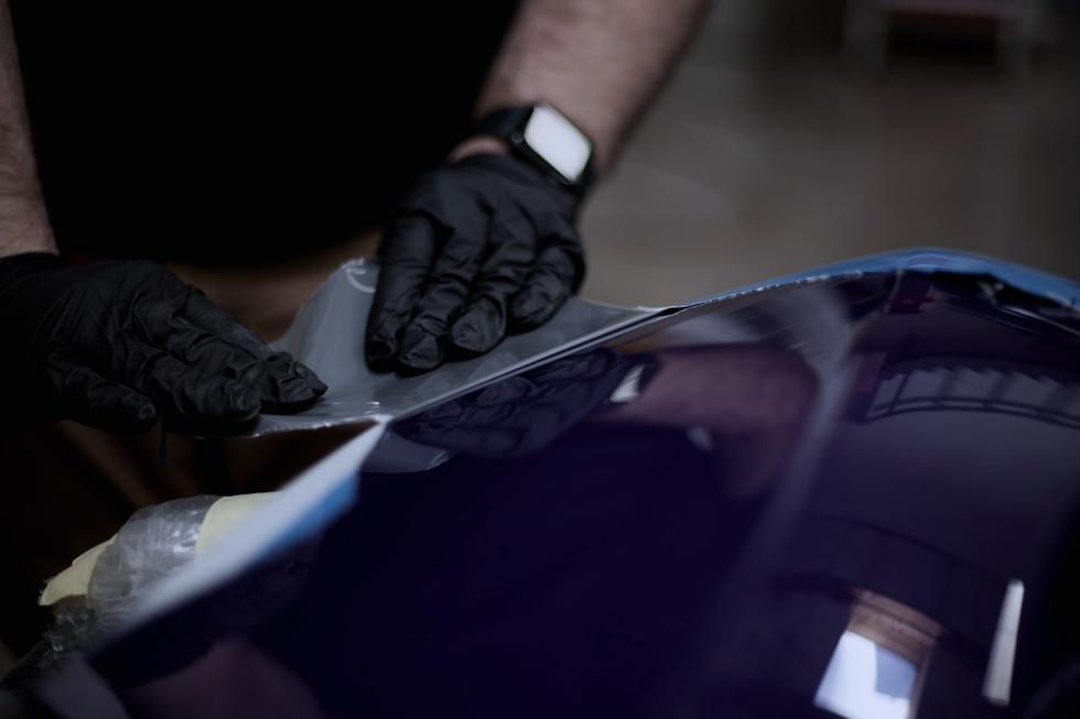 Gloved hands working film across a car panel