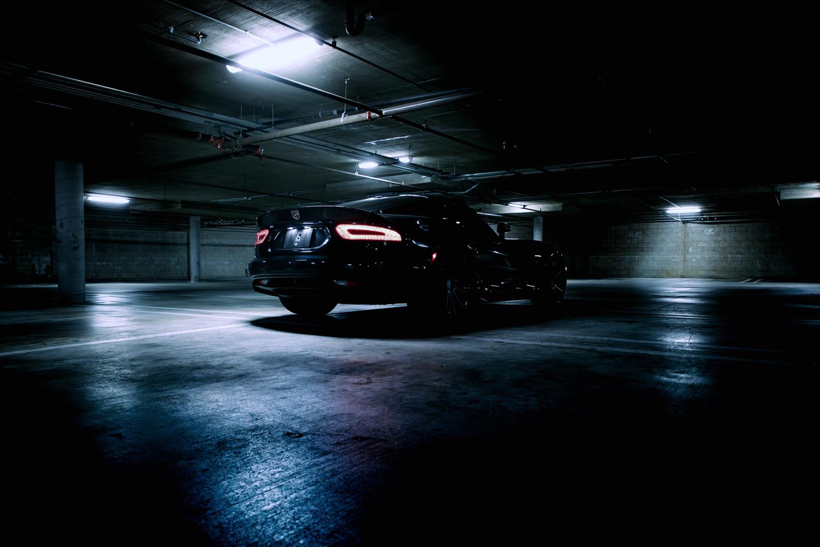 Dark car parked under strip lighting in a concrete garage